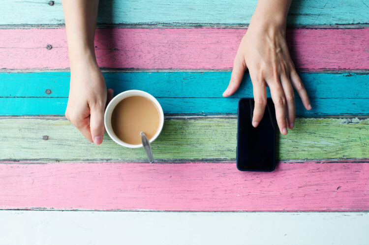 Hand holding coffee cup and mobile phone